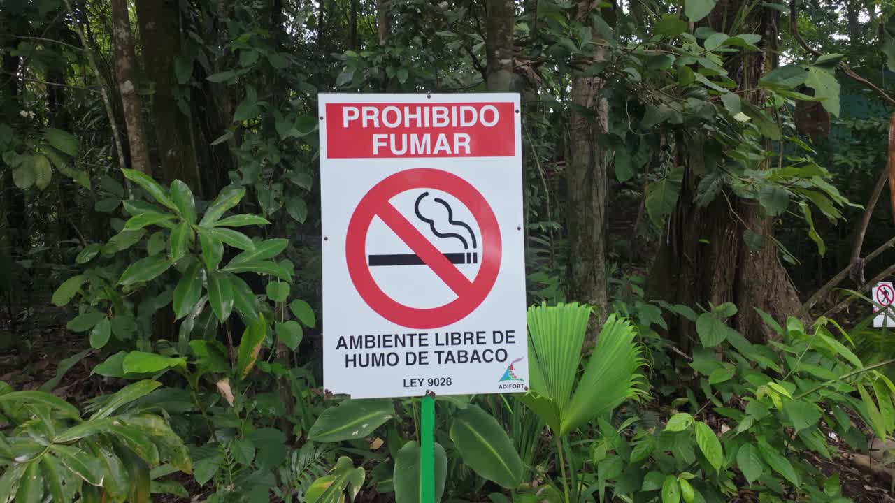 A bright red no smoking sign with a dense rainforest in the background at Fortuna Waterfall in Costa Rica