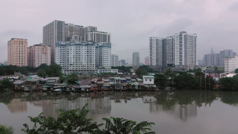 Early-foggy,smoggy-morning-crane-shot-drone-footage-over-canal-and-urban-waterfront-areas-of-Saigon,-Ho-Chi-Minh-City,-Vietnam