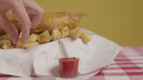 people using fingers to eat traditional british takeaway meal of fish and chips with vinegar