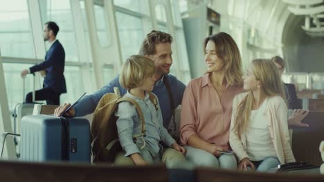 foto de retrato de la linda familia feliz con hijo e hija sentados en el aeropuerto con maletas y sonriendo a la cámara mientras esperan su partida