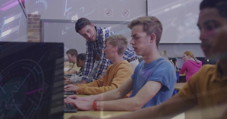 Instructor moving lab row, leaning over student, pointing at monitor, students typing for help