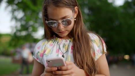 close up of serious girl playing games on phone. girl with phone in summer park