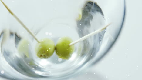 white spots floating over close up of olives in cocktail glass against grey background
