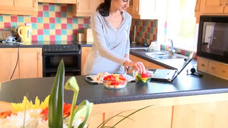 mujer hermosa preparando una ensalada y mirando una computadora portátil