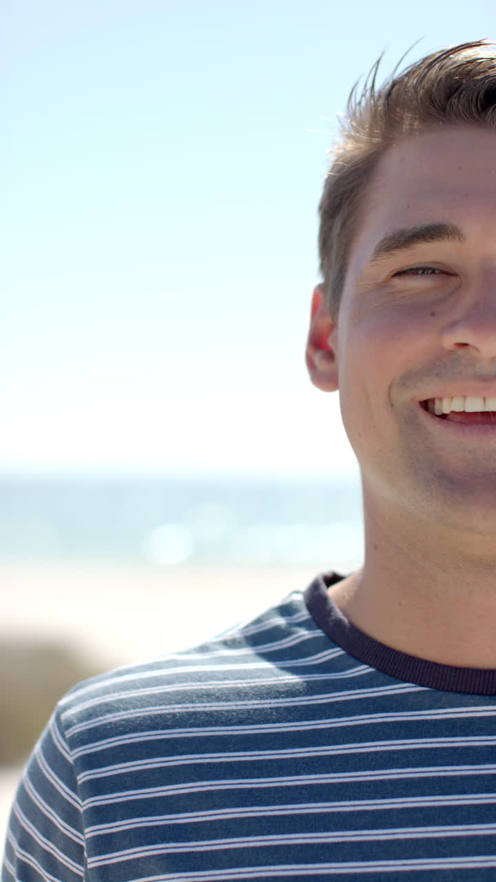 Vertical video: Smiling man enjoying sunny day at beach, wearing striped shirt