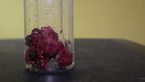 mixed frozen berries dropped inside the wet transparent glass container- eye-level shot