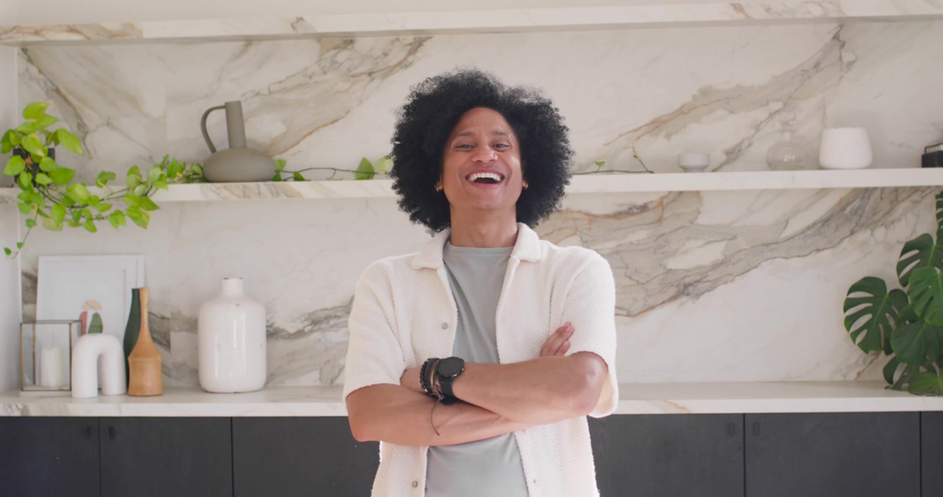 Afro-Amerikaanse man met gekruiste armen, lachend met een brede glimlach bij een marmeren achterwand.
