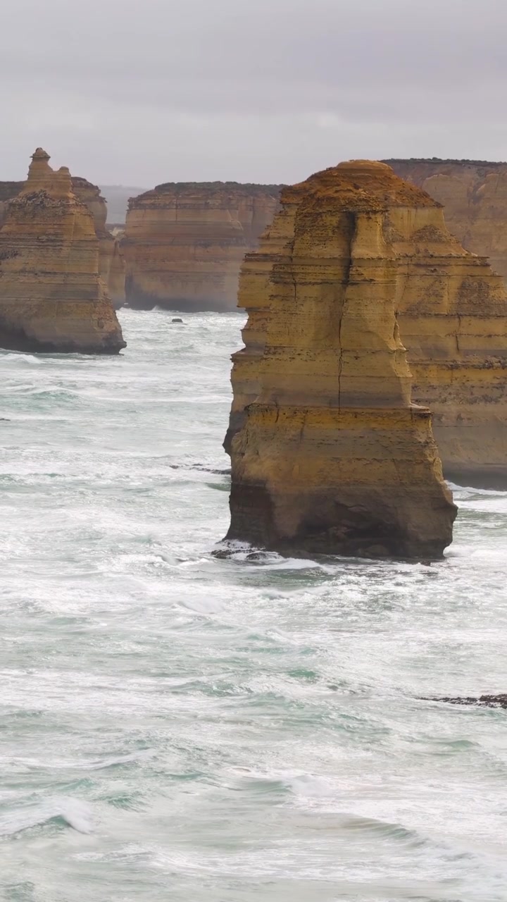 The Twelve Apostles rock formations stand against turbulent ocean waves under overcast skies at Port Campbell, Australia