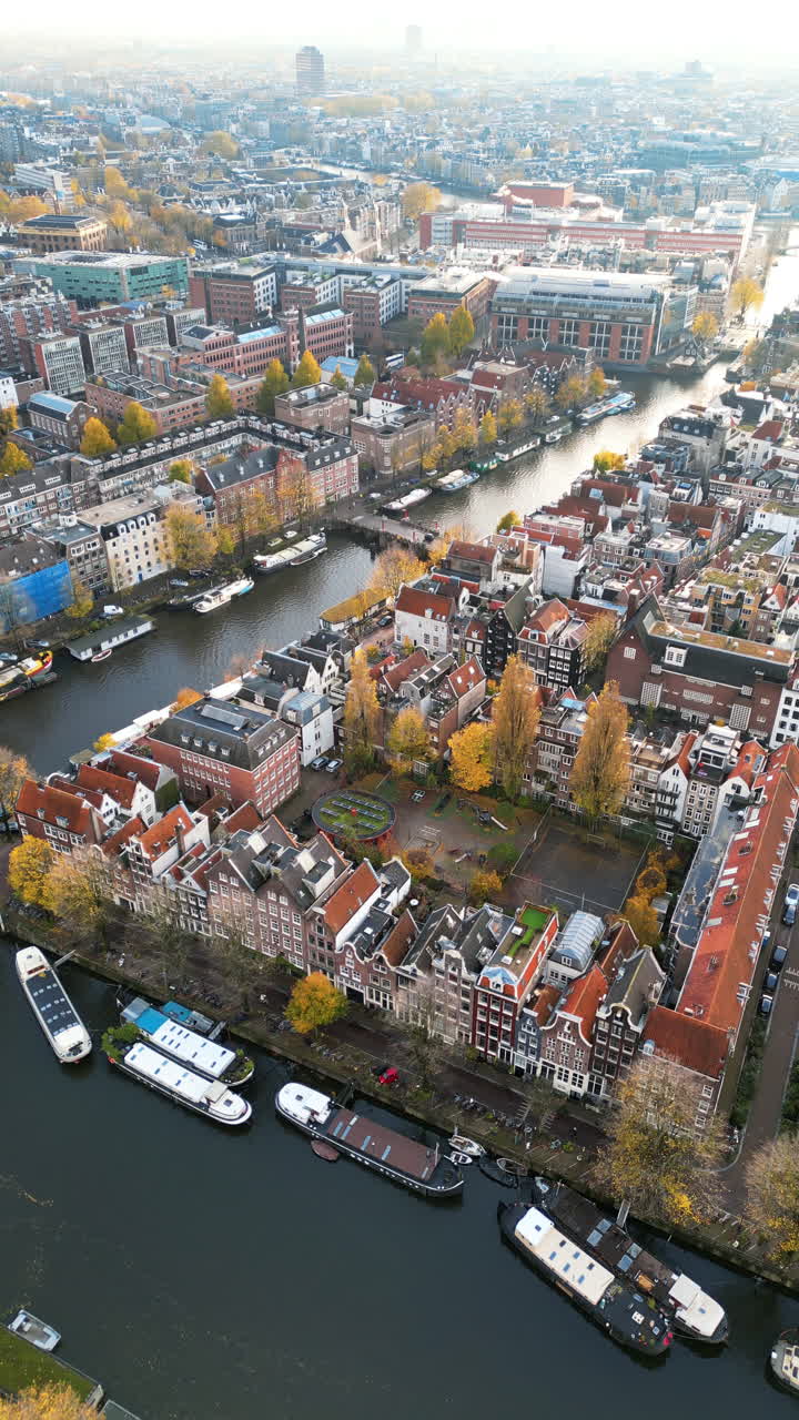 Aerial drone view of buildings surrounding a tree-lined canal in Amsterdam, Netherlands in daylight. Vertical
