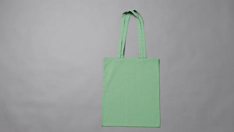 Primer-Plano-De-Una-Bolsa-Verde-Sobre-Fondo-Gris,-Con-Espacio-Para-Copiar,-Cámara-Lenta