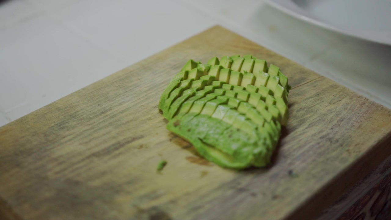 Vista em close-up de abacate fatiado cuidadosamente arranjado em uma tábua de corte de madeira, textura verde fresca destacando um ingrediente saudável usado na culinária e no preparo de refeições.