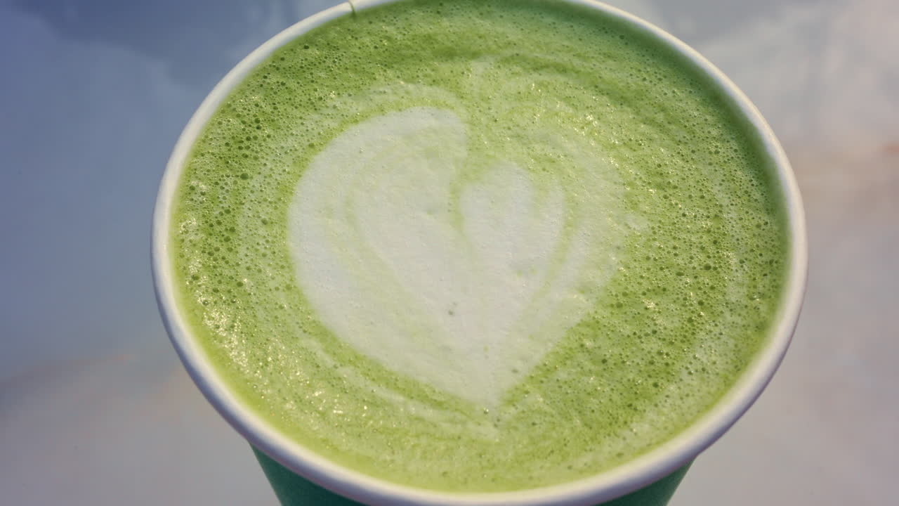 Vista superior em close-up de um latte matcha verde com arte latte em forma de coração num copo para viagem