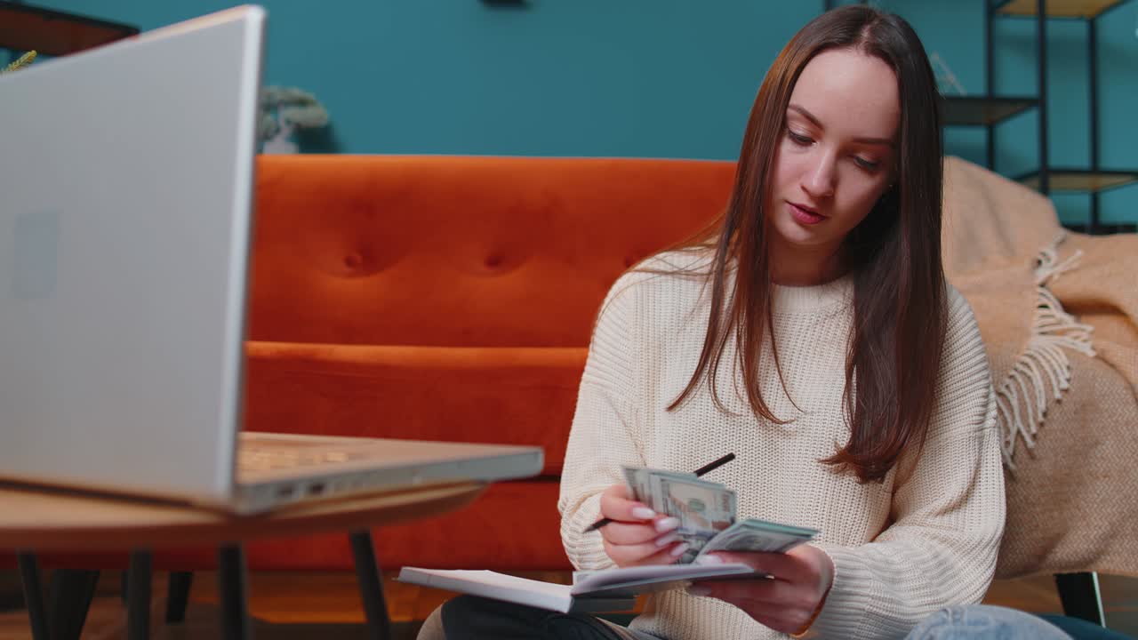 Donna che pianifica il budget domestico sul laptop e conta denaro, una ragazza che controlla il reddito in contanti in dollari.