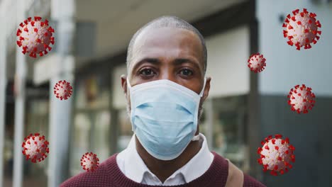 animation of falling covid 19 cells over african american man wearing face mask