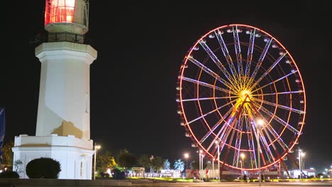 ferris wheel near the lighthouse rotates at night on the batumi embankment