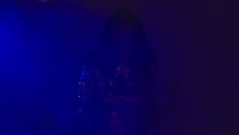 primer plano de una mujer en un bar nocturno o discoteca bailando y divirtiéndose mirando a la cámara con hielo seco