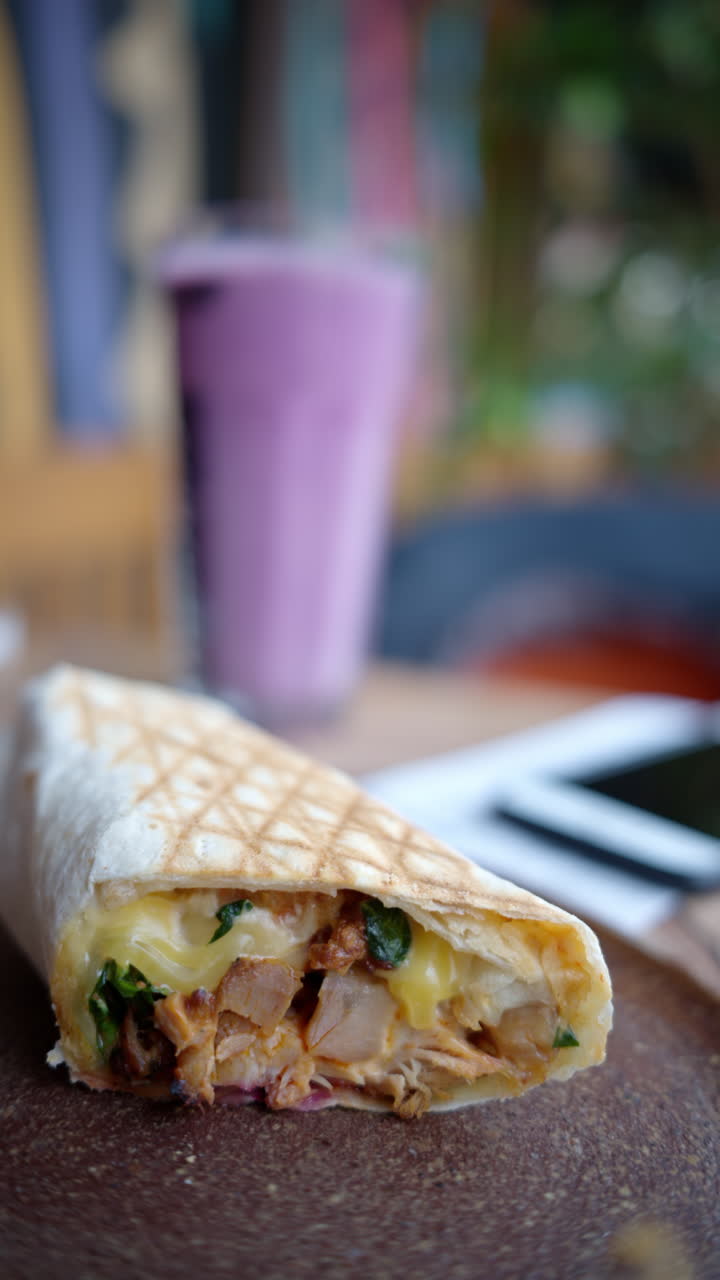 Close-up of cut up wrap on the table, with a smoothie on the background. Vertical
