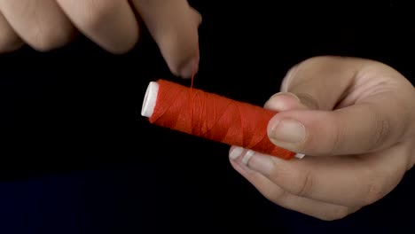 winding red sewing thread on spool with both hands