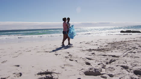 Pareja-Afroamericana-Caminando-Con-Sacos-De-Basura-Y-Recogiendo-Basura-De-La-Playa