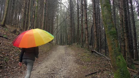 young-sporty-female-walks-in-dark-forest-holding-colourful-umbrella,-slow-motion