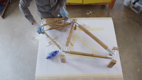 overhead shot of male craftsman in workshop assembling hand built sustainable bamboo bicycle frame