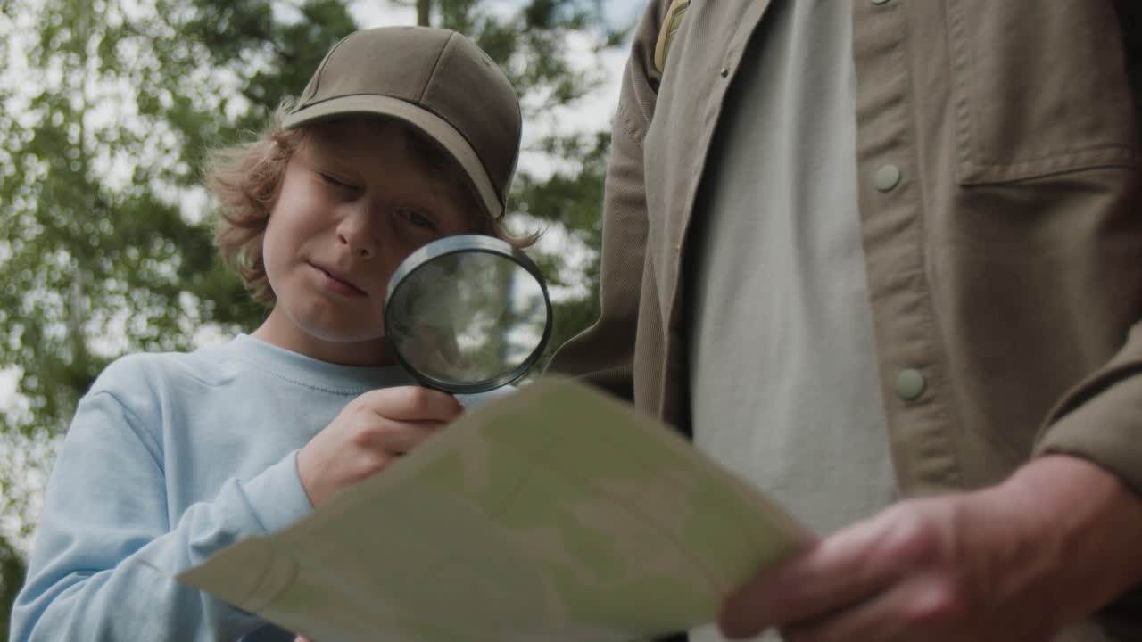 Child uses magnifying glass to examine map with parent