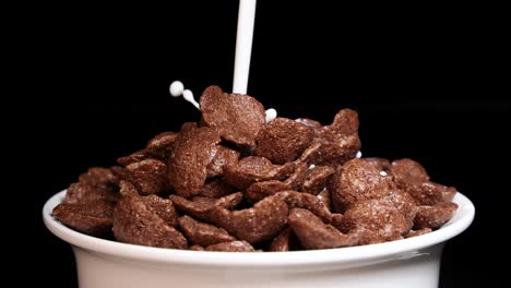 milk cascades over crunchy chocolate cereal in a white bowl against a black background, creating a dynamic splash effect