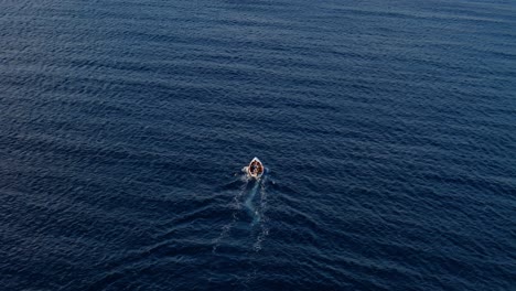 High-angle-aerial-rearview-of-fishermen-driving-small-red-white-boat-in-deep-dark-blue-ocean-water,-Curacao