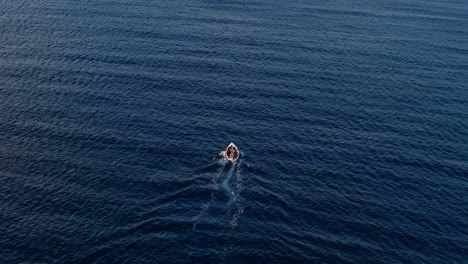 high angle aerial rearview of fishermen driving small red white boat in deep dark blue ocean water, curacao