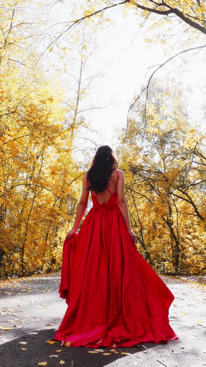 Una scena affascinante che ritrae una donna con un vestito rosso fluttuante, circondata da un vivace fogliame autunnale, che mette in mostra la bellezza della natura e l'eleganza in armonia