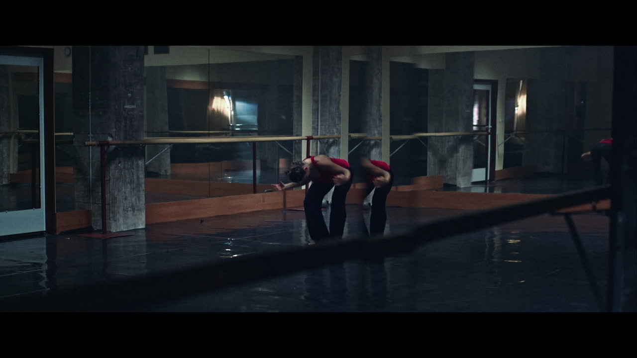 A young woman practices modern dancing and ballet in a moody room full of mirrors