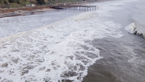 Strong-stormy-waves-and-Seacliff-pier-across-Santa-Cruz-coastline-after-bomb-cyclone-storm-damage,-Aerial-orbiting-view