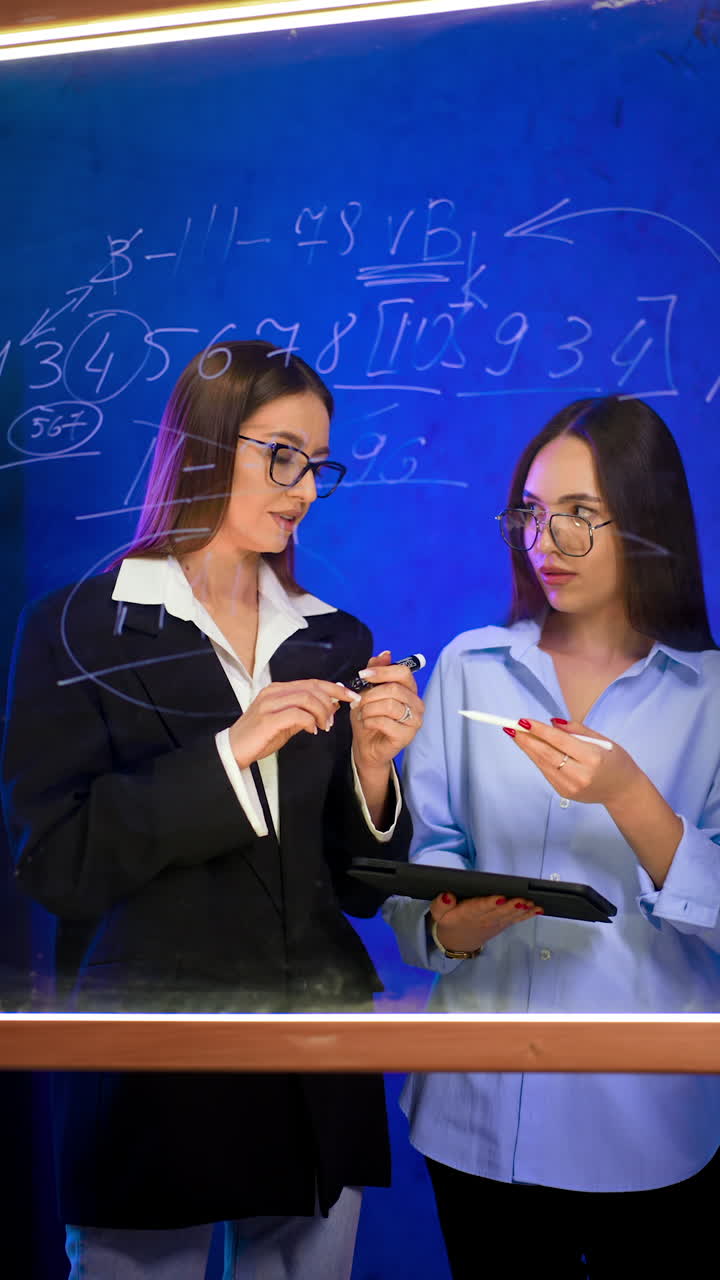 Attractive Caucasian ladies checking numbers written on the glass wall. Women communicate, look at clipboard and nod agreeing with each other. Vertical video.