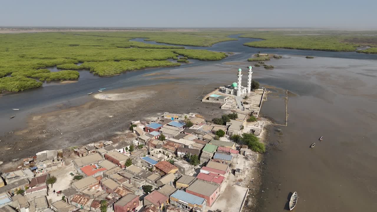Drone aerial of Joal mosque in Senegal with tall white minarets, surrounded by lagoon and coastal village in Africa