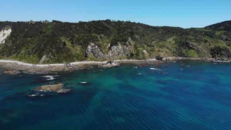 Mangawhai-Heads-aerial-shot-on-a-sunny-day,-from-the-sea-in-a-distance-towards-the-mountain-revealing-the-foreshore