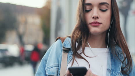 vista de cerca de una joven caucásica con auriculares escuchando música en un smartphone, cantando y bailando en la calle