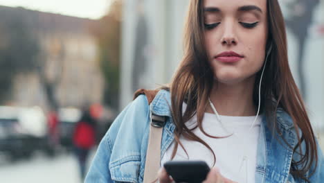 close-up view of young caucasian woman in headphones listening to the music on smartphone, singing and dancing in the street