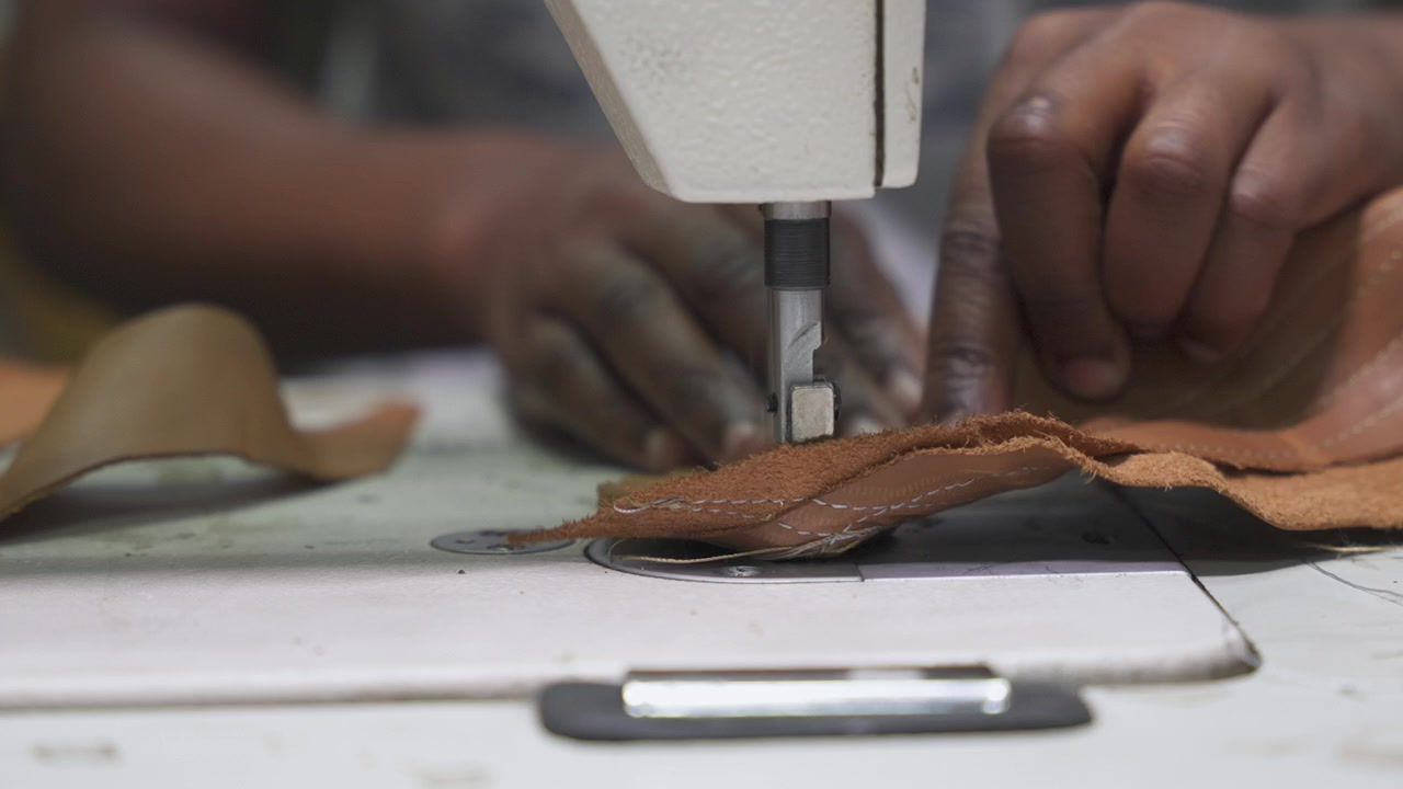 Close-up of shoe maker crafts unique leather footwear, expertly using sowing machine. Perfect for documentary showing artisan at work.