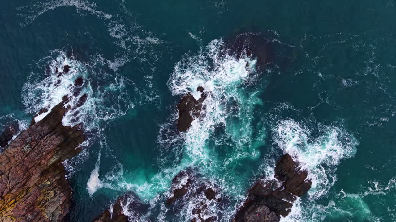 Onde che si infrangono contro le rocce frastagliate in un paesaggio costiero illuminato dalla luce del sole