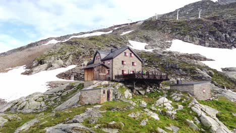 House-surrounded-by-stones-and-a-few-snow-fields-with-a-rope-way-in-the-background-in-the-Alps-in-Kaernten,-Austria