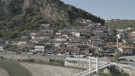 Drone-shot-of-the-city-of-Berat-and-its-castle-and-fortress-in-Albania,-the-city-of-a-thousand-windows-on-a-sunny-day-in-the-valley-with-blue-sky-with-white-houses-near-the-mountains-LOG