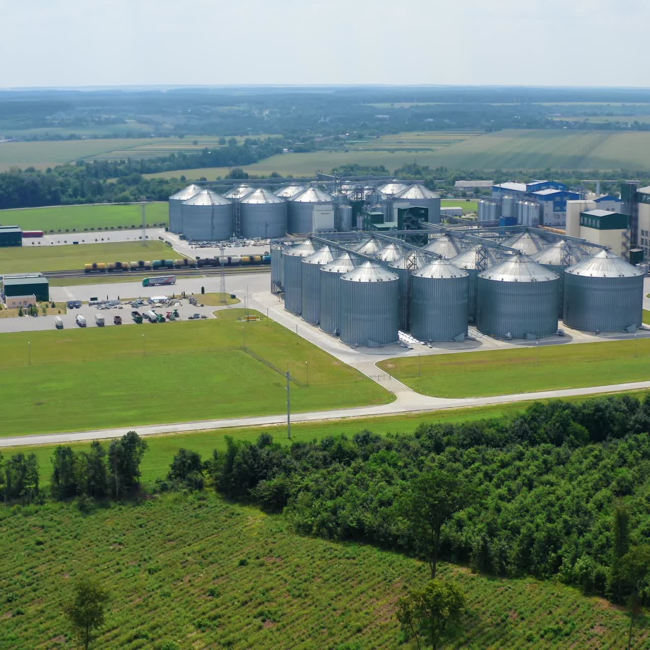 Moderne Agrarverarbeitungsanlage. Getreidesilos auf grünem Feld. Großes Gelände mit metallenen Saatgutsilos auf dem Land an einem sonnigen Sommertag. Luftaufnahme.