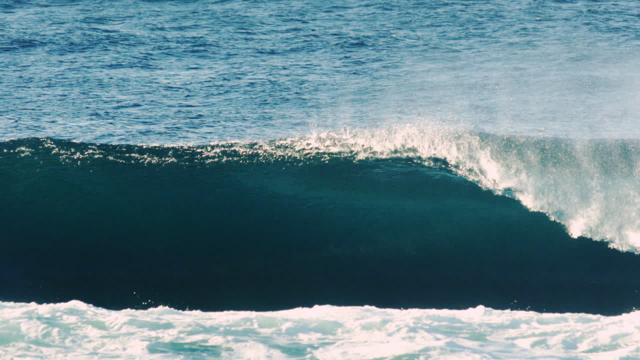 Blue ocean wave swells forward under daylight with strong ripple texture and crest