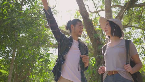 young asian man and caucasian woman friend traveling in the forest together. they are feeling fresh and relax in nature wild, looking and pointing the view then continue walking with happiness and fun