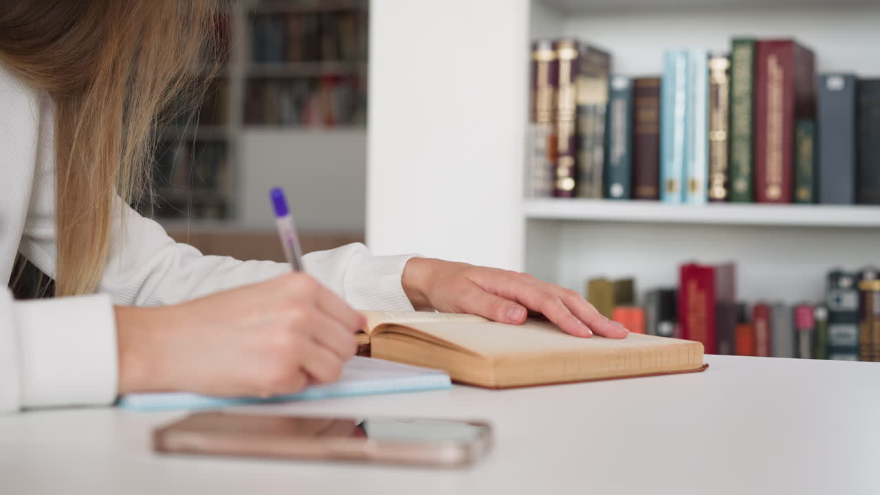estudiante reescribe la información del libro en el cuaderno. joven se prepara para un seminario en la biblioteca de la universidad. obtener educación superior