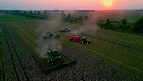 Aerial-drone-backward-moving-shot-over-combine-harvesters-and-tractors-harvesting-and-collecting-grains-on-an-autumn-evening