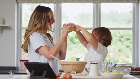 mother and son in pyjamas making funny faces with lemons as they bake in kitchen at home together