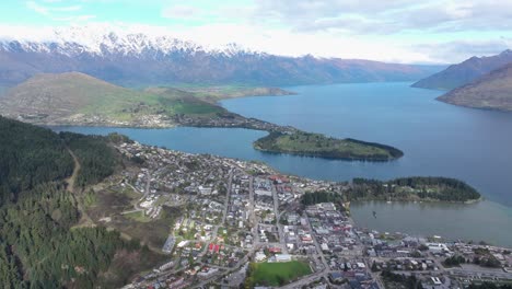 Birds-eye-view-of-village-on-lakeshore,-peninsula-and-snowy-mountain-range