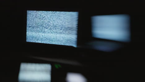 a side angle shot with selective focus of four digital computer device screens displaying a choppy static noise pattern in a dark room