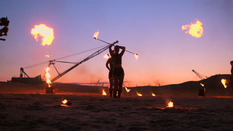 professional artists show a fire show at a summer festival on the sand in slow motion. fourth person acrobats from circus work with fire at night on the beach